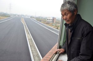 An old man looks down from his house which stands alone in the middle of a newly built road in Wenling, Zhejiang province